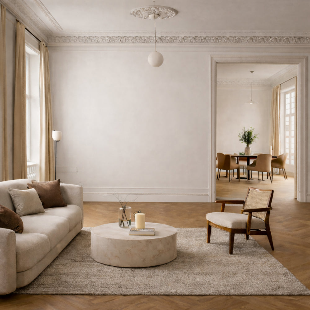 Salon avec canapé beige, table basse ronde, fauteuil en bois et salle à manger en arrière-plan