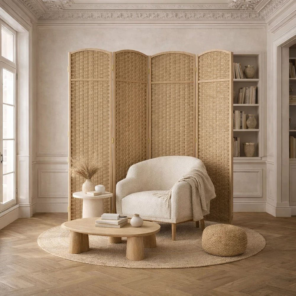 Un salon avec un fauteuil blanc, une table basse en bois, un paravent en rotin et une bibliothèque